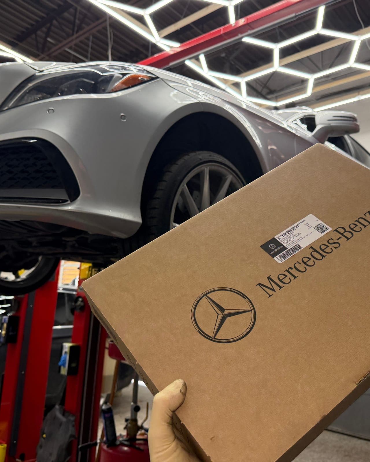 Mercedes-Benz on a two-post lift with OEM parts in the foreground.